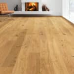photo vue au ras du sol qui met en valeur un parquet à planches larges, couleur claire, dans un salon avec cheminée allumée