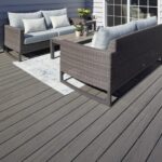 photo d'un salon de jardin en plastique gris tressé et habillé d'assises et de coussins blanc, avec un tapis blanc au sol, conçu en lames grises composites.