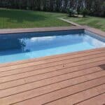 photo d'un jardin parfaitement tondu avec une piscine en premier plan, entourée d'une terrasse en bois