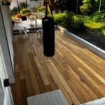 photo d'une terrasse ombragée avec un punching ball pendu au plafond au milileu et entourée d'un petit jardin arboré