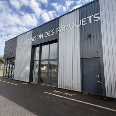 photo d'une façade de magasin de parquets prise de biais avec une entrée en baie vitrée et des murs en tôle grise et blanche.