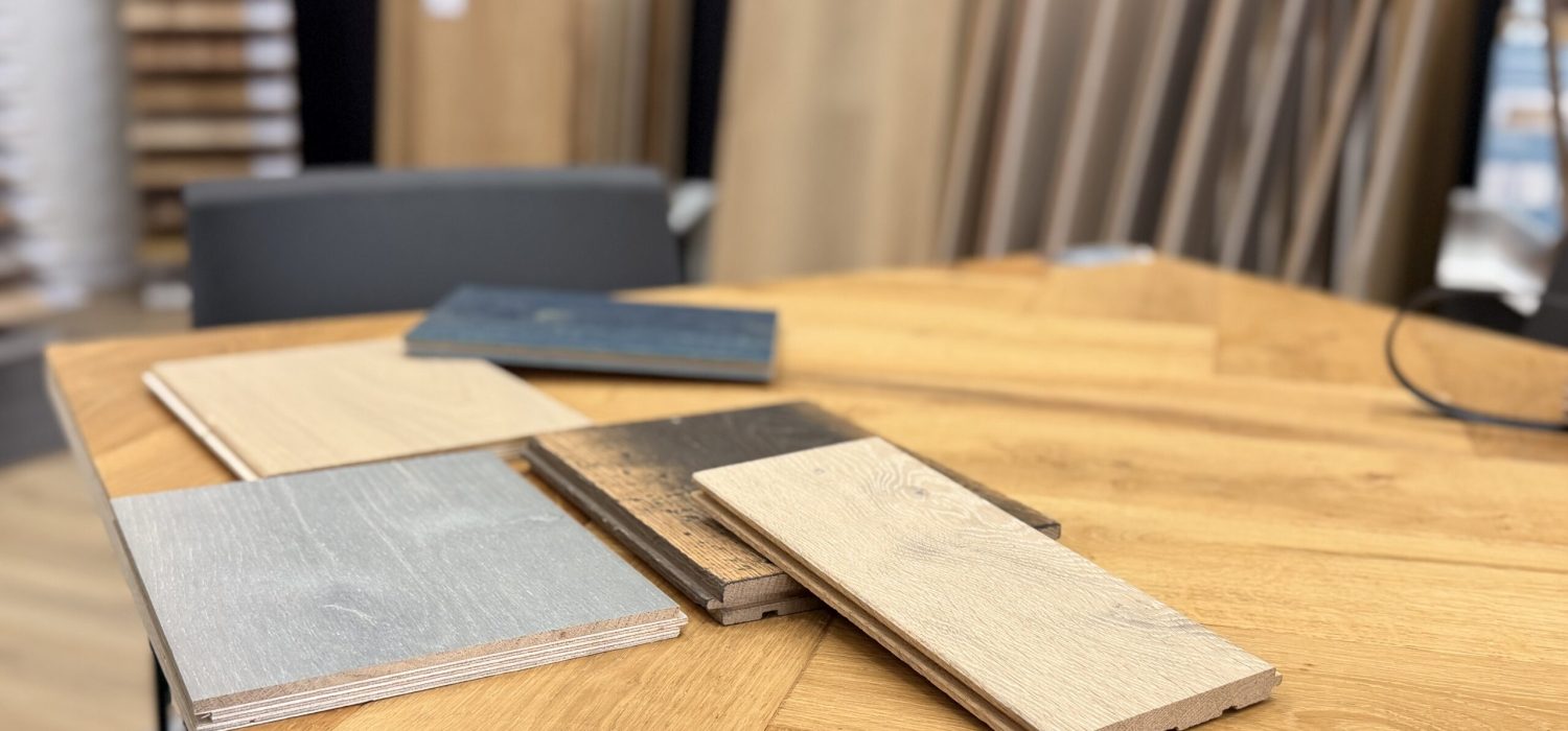 photo de morceaux de lames de parquets de toutes les couleurs, posés sur une table. En arrière-plan, le showroom du magasin avec des échantillons de grande taille.